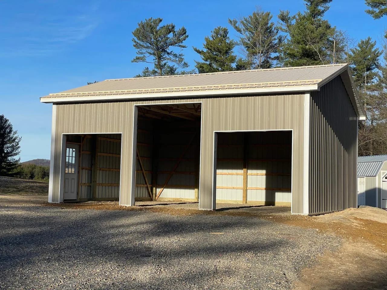 Completed tan post-frame building with three open bays and a walk-in door